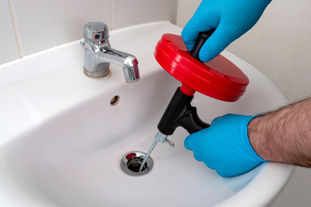 mage of a plumber using a drain snake to clear a clogged drain